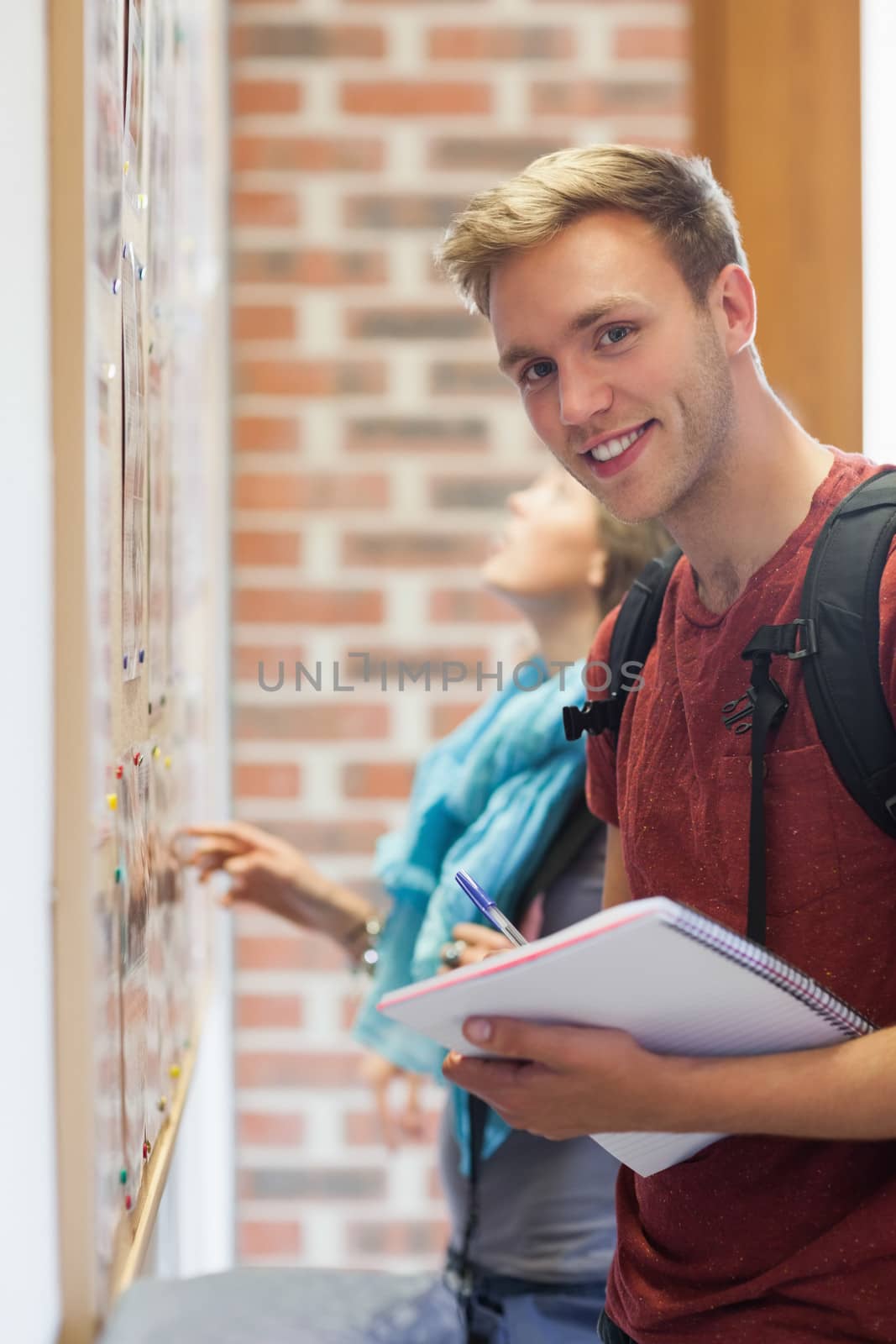 Cheerful student searching something on notice board by Wavebreakmedia