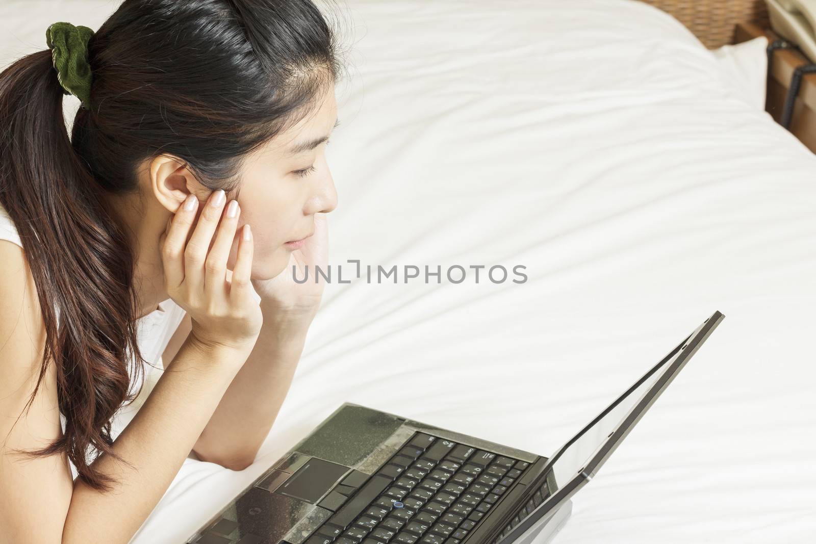 happy young asian woman working with laptop in bedroom by FrameAngel