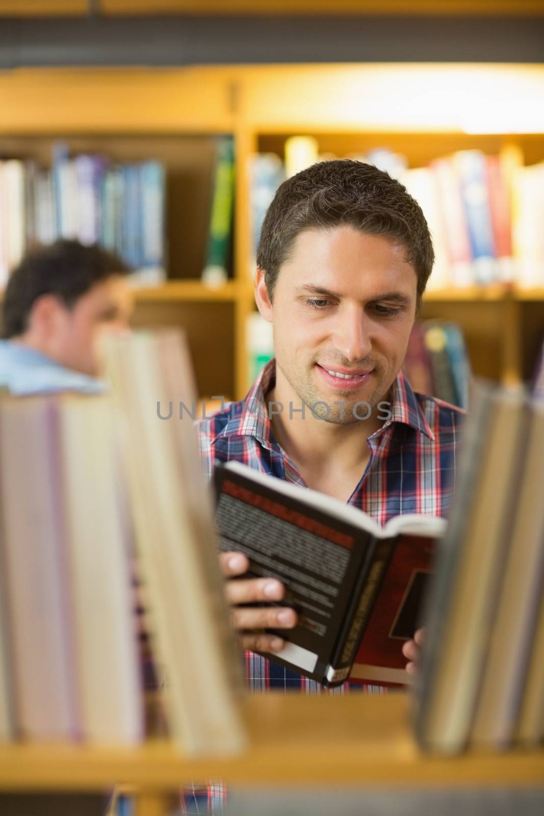 Mature student reading book by shelf in the library by Wavebreakmedia