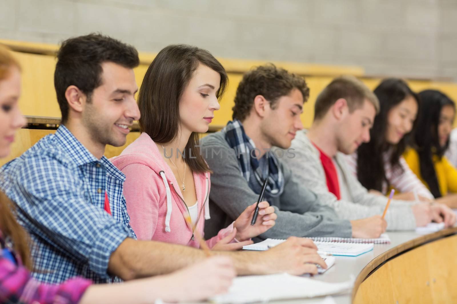 Students writing notes in a row at the lecture hall by Wavebreakmedia