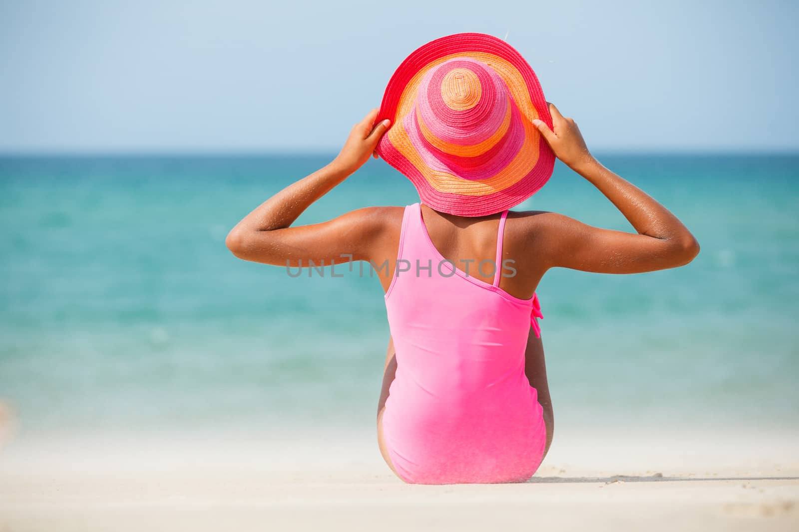 Back view of a cute little girl in pink hat at tropical beach