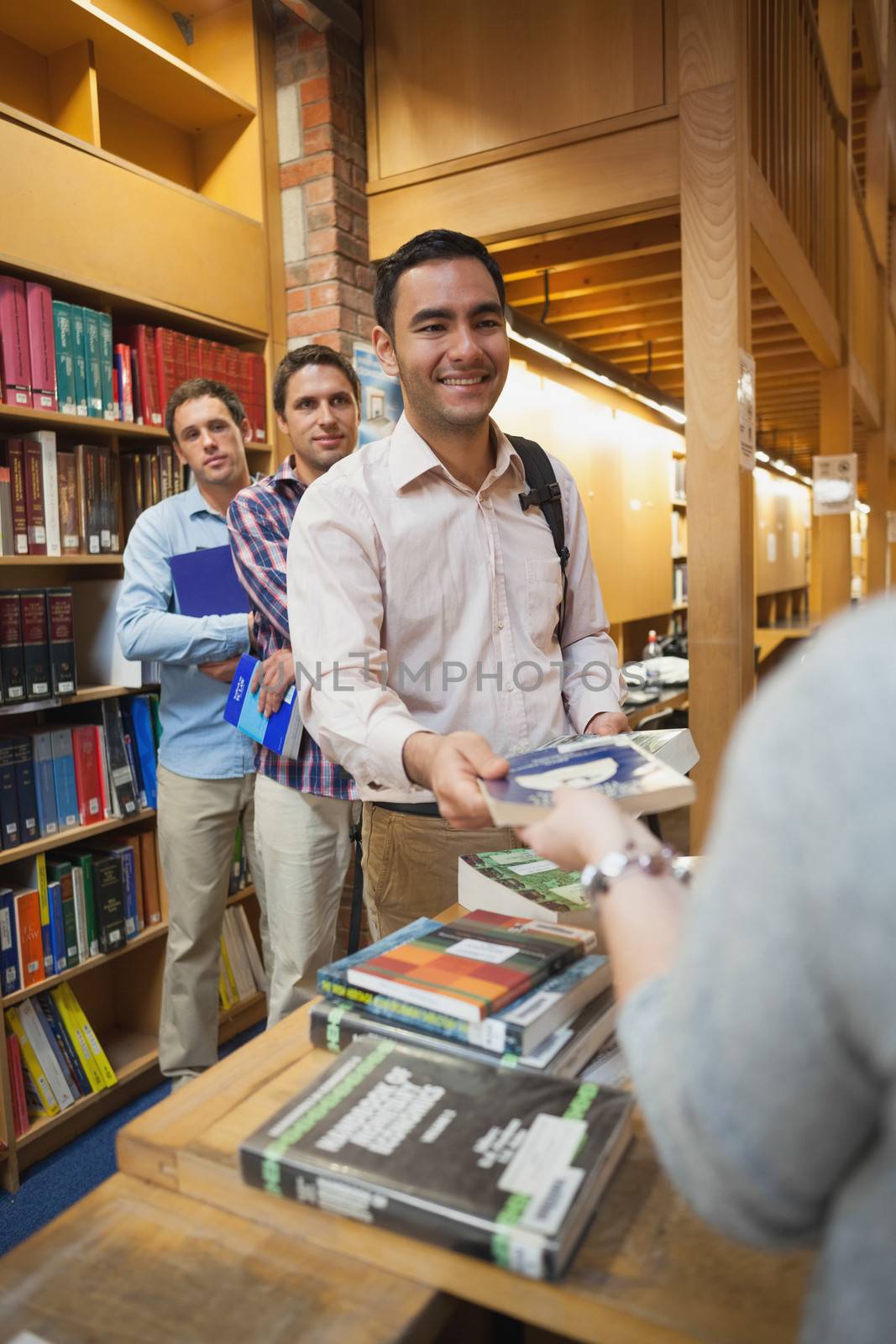 Attractive man handing a book to the female librarian in library