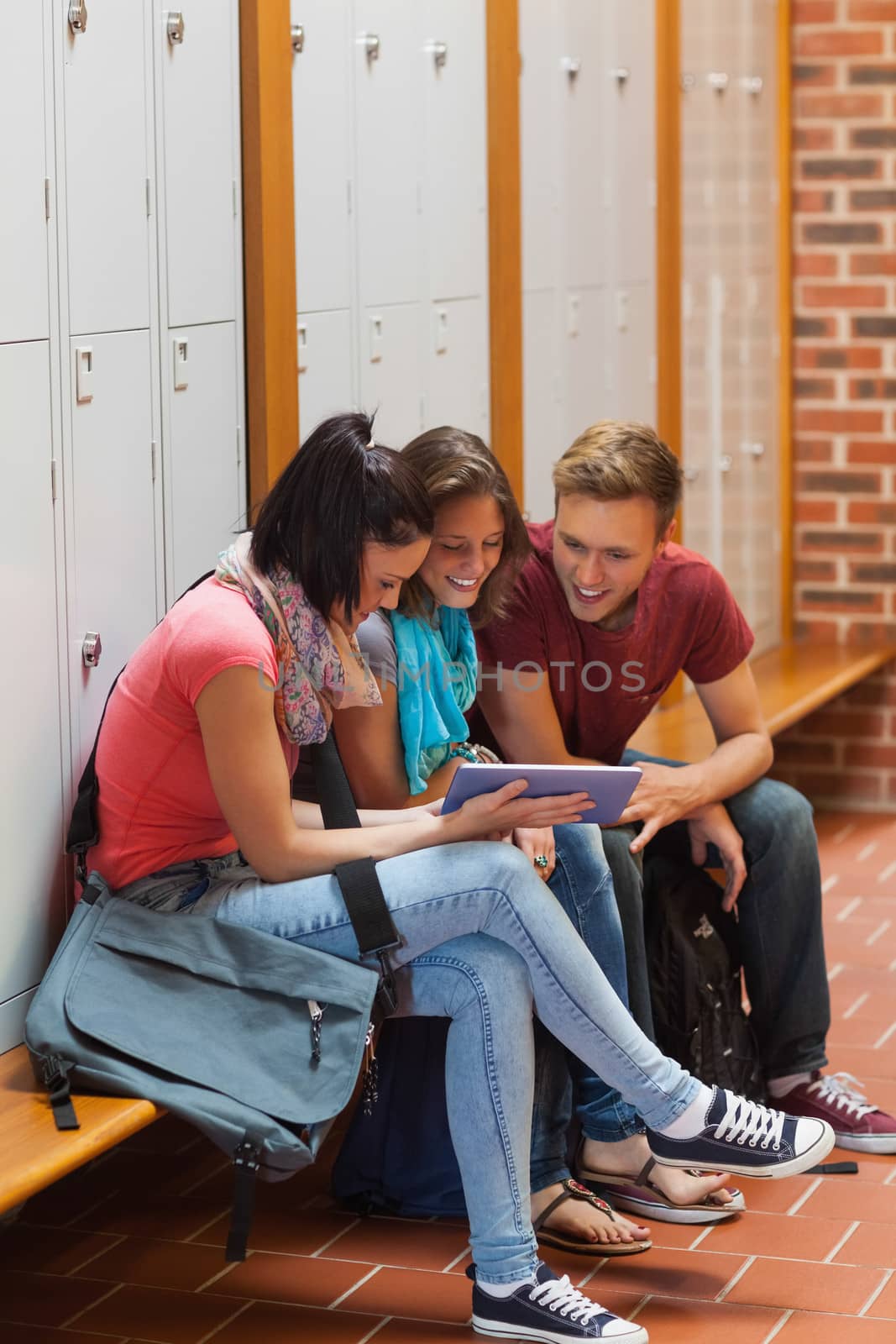 Smiling students sitting on bench using tablet in school