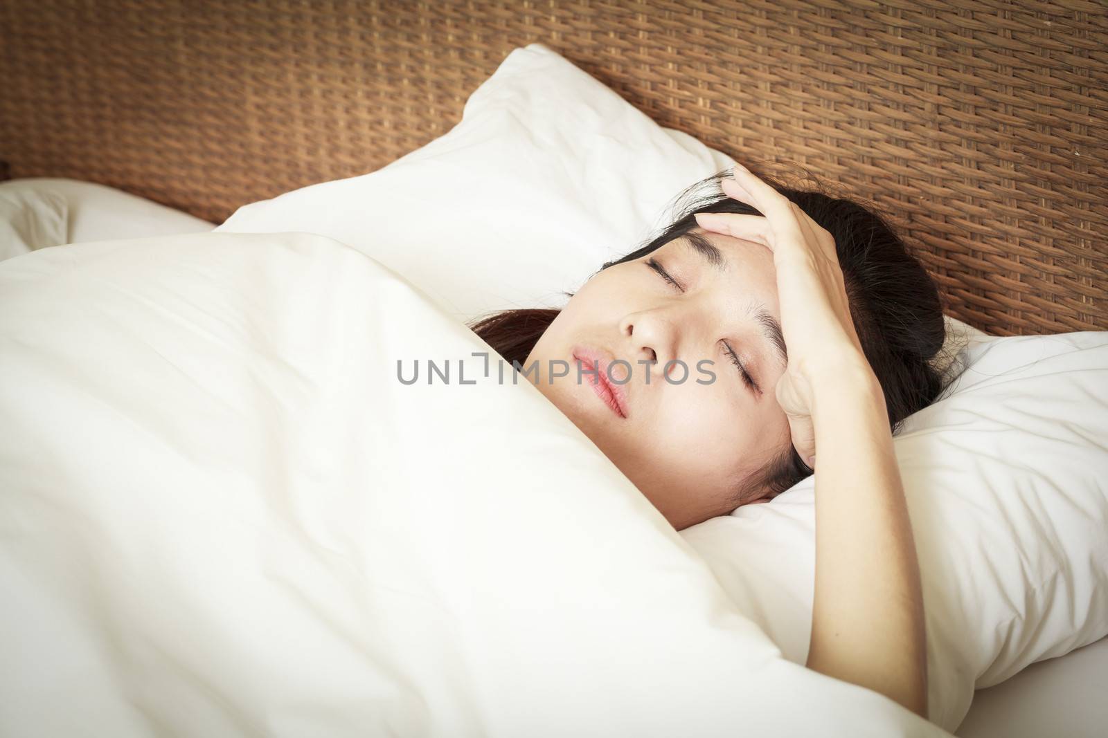 woman with headache lying on bed by FrameAngel