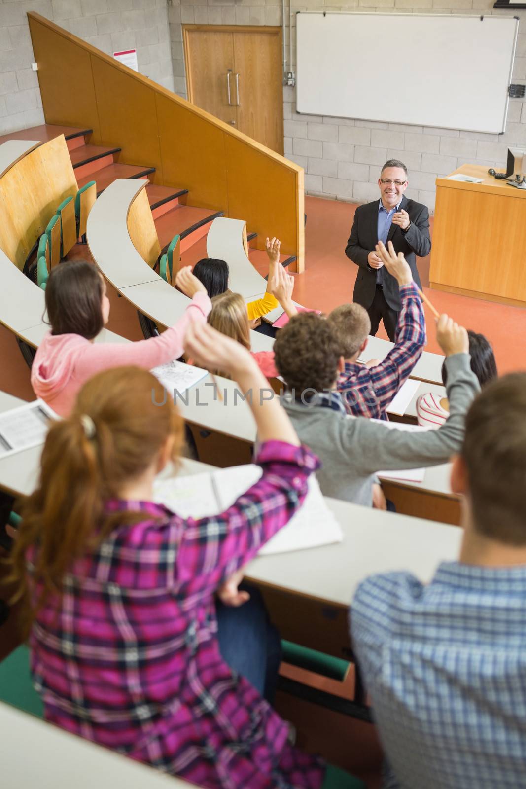 Students raising hands with a teacher in the lecture hall by Wavebreakmedia