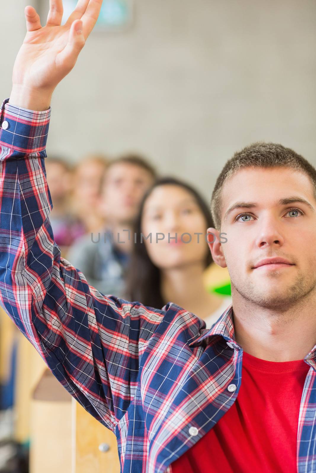 Close up of a young male student raising hand by others in a row at the classroom
