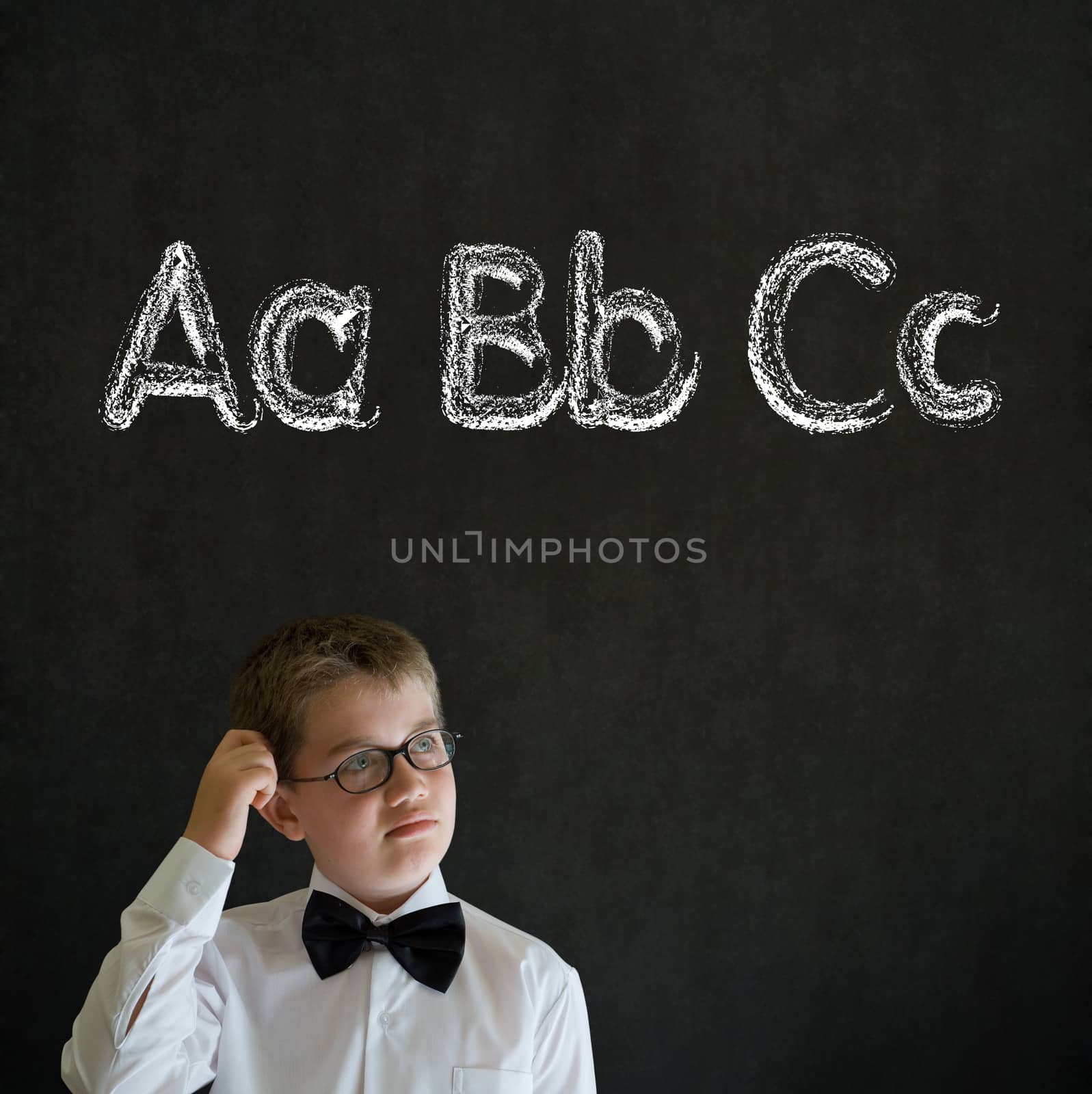 Scratching head thinking boy dressed up as business man with learn English language alphabet on blackboard background