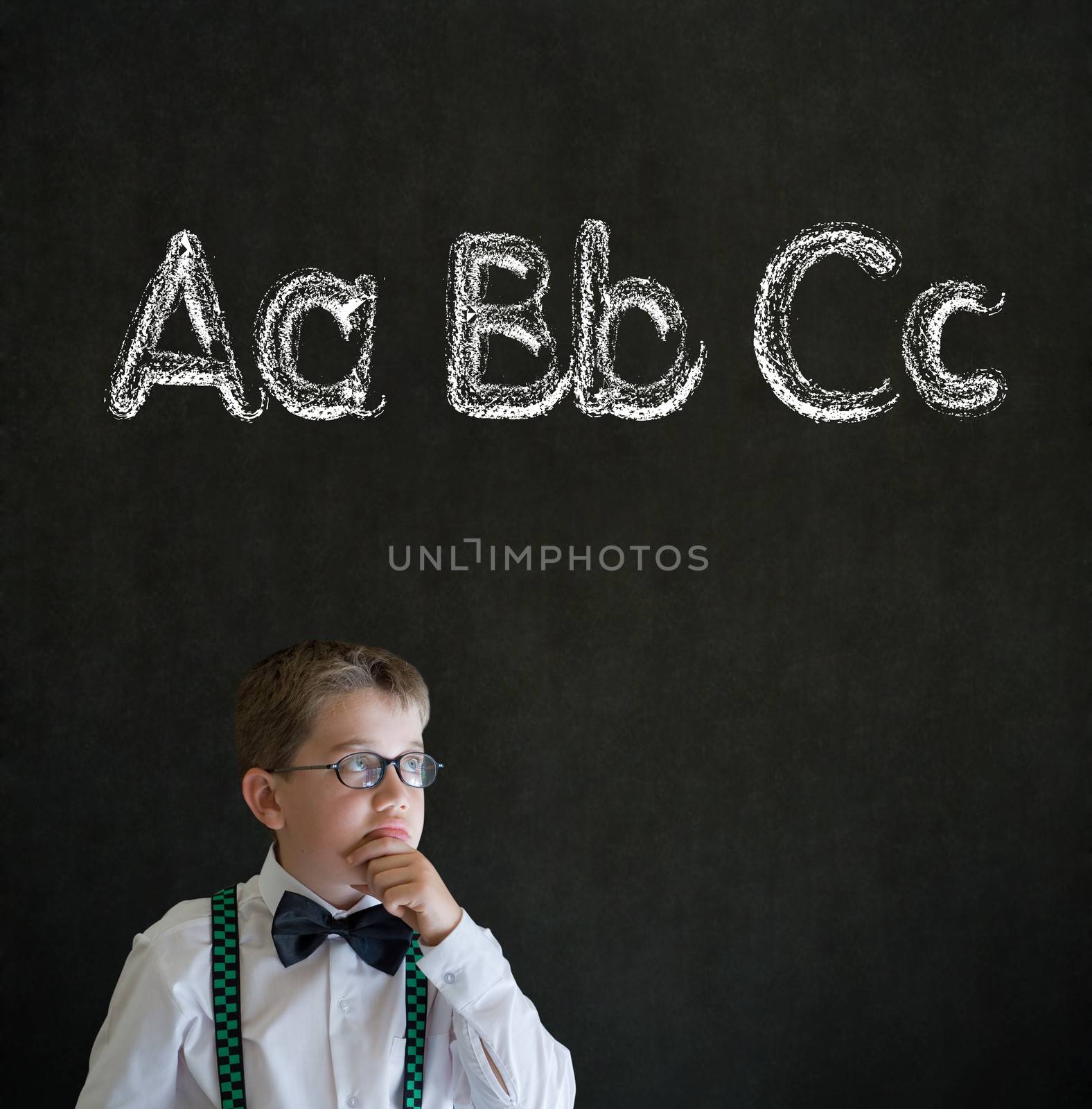 Thinking boy dressed up as business man with learn English language alphabet on blackboard background