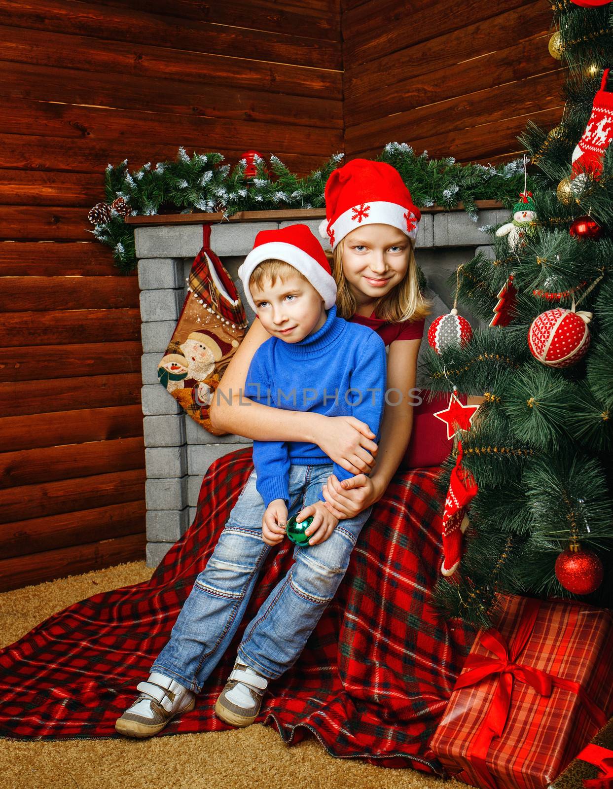 Girl hugs her little brother near Christmas tree