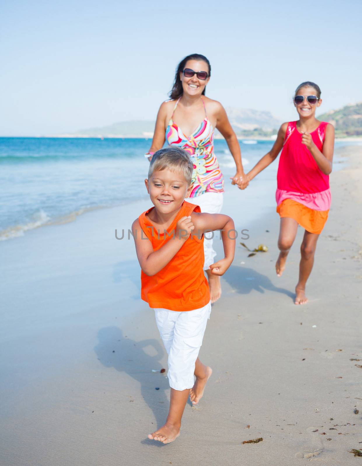 Adorable happy boy with sister and mother running on beach