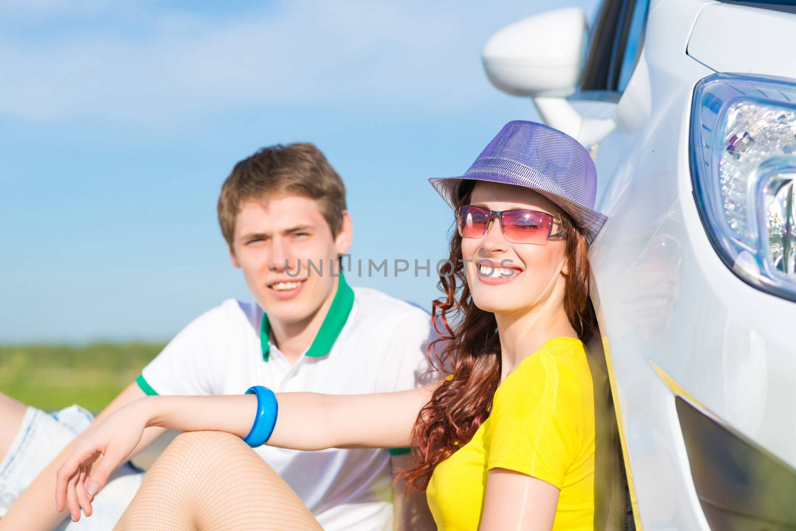 young couple sitting on the ground next to the wheel of a car, a summer road trip