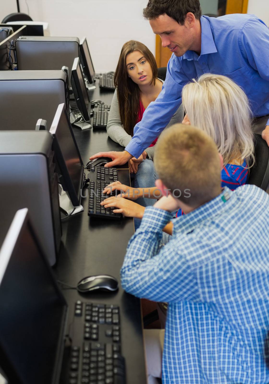 Side view of a teacher explaining to young college students in the computer room