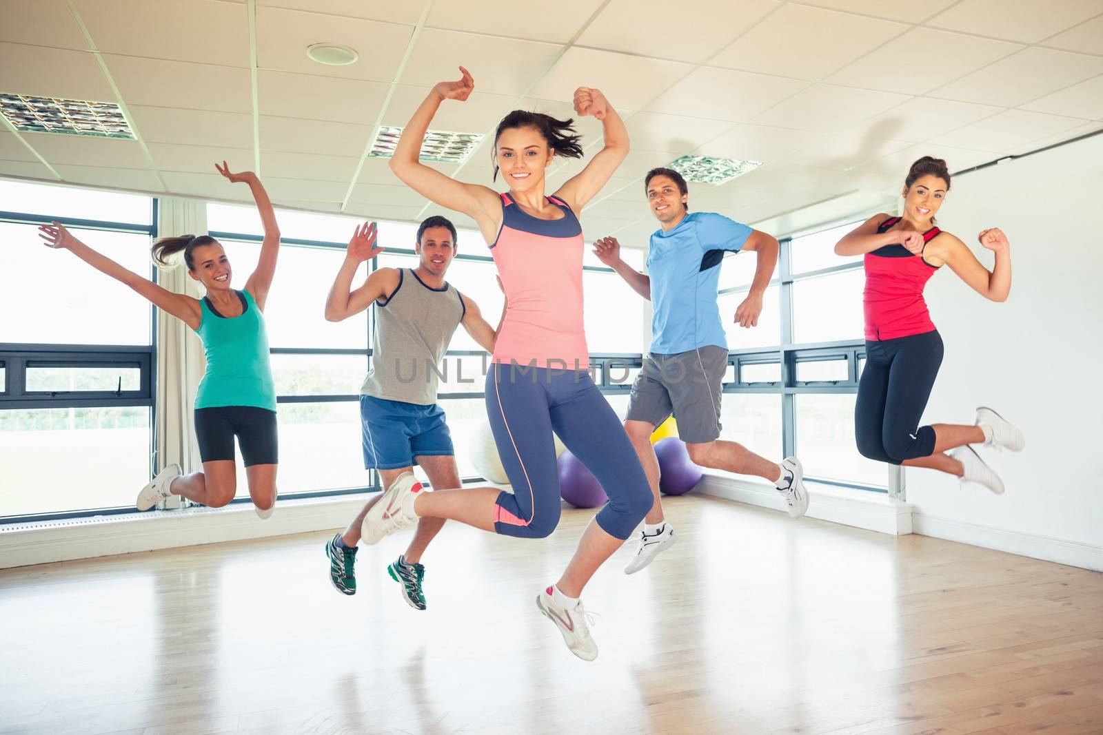 Fitness class and instructor jumping in fitness studio by Wavebreakmedia