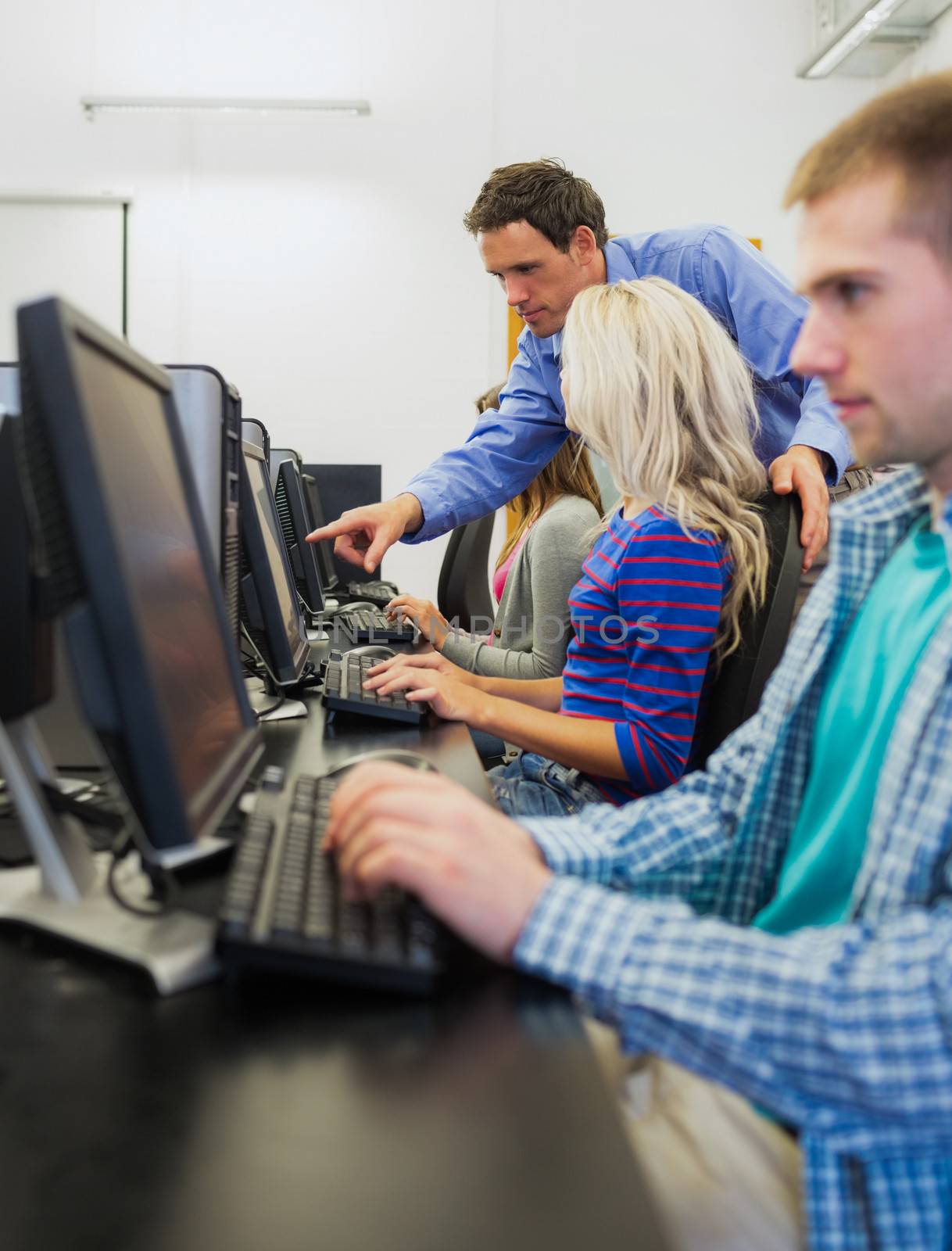 Side view of teacher showing something on screen to student in the computer room