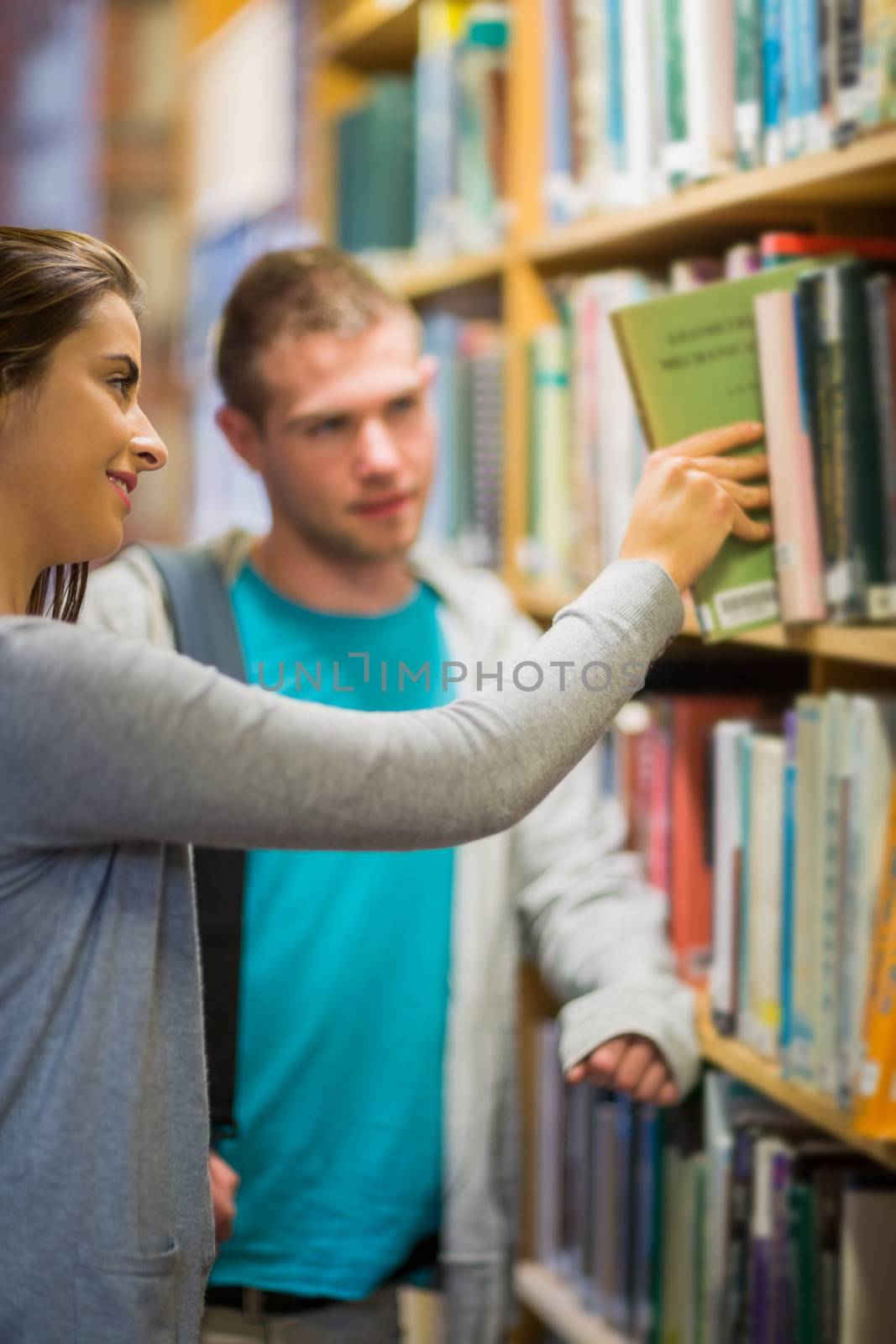 Blurred young male looking at female select a book from bookshelf in the library