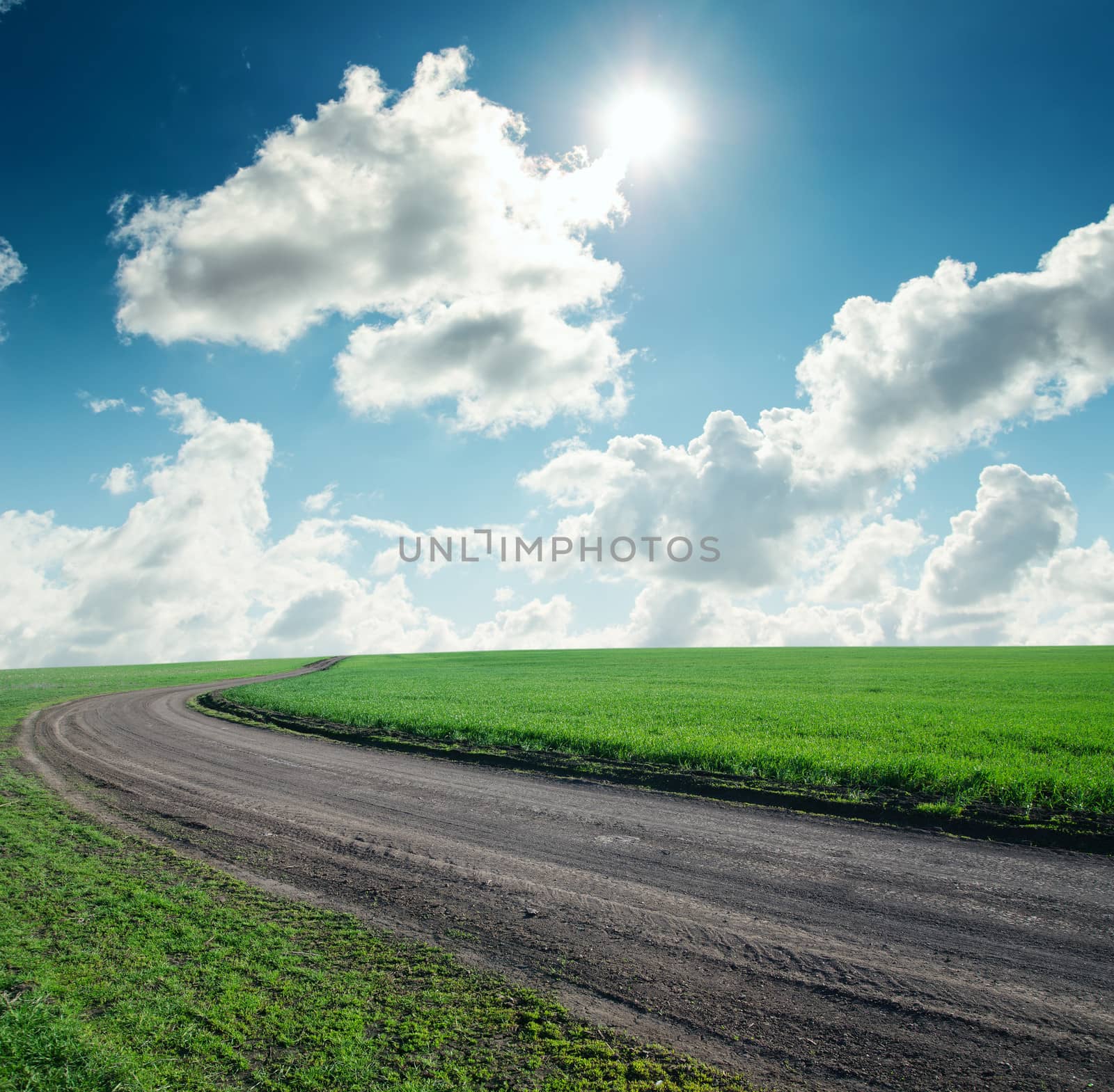 road in green grass under cloudy sky with sun