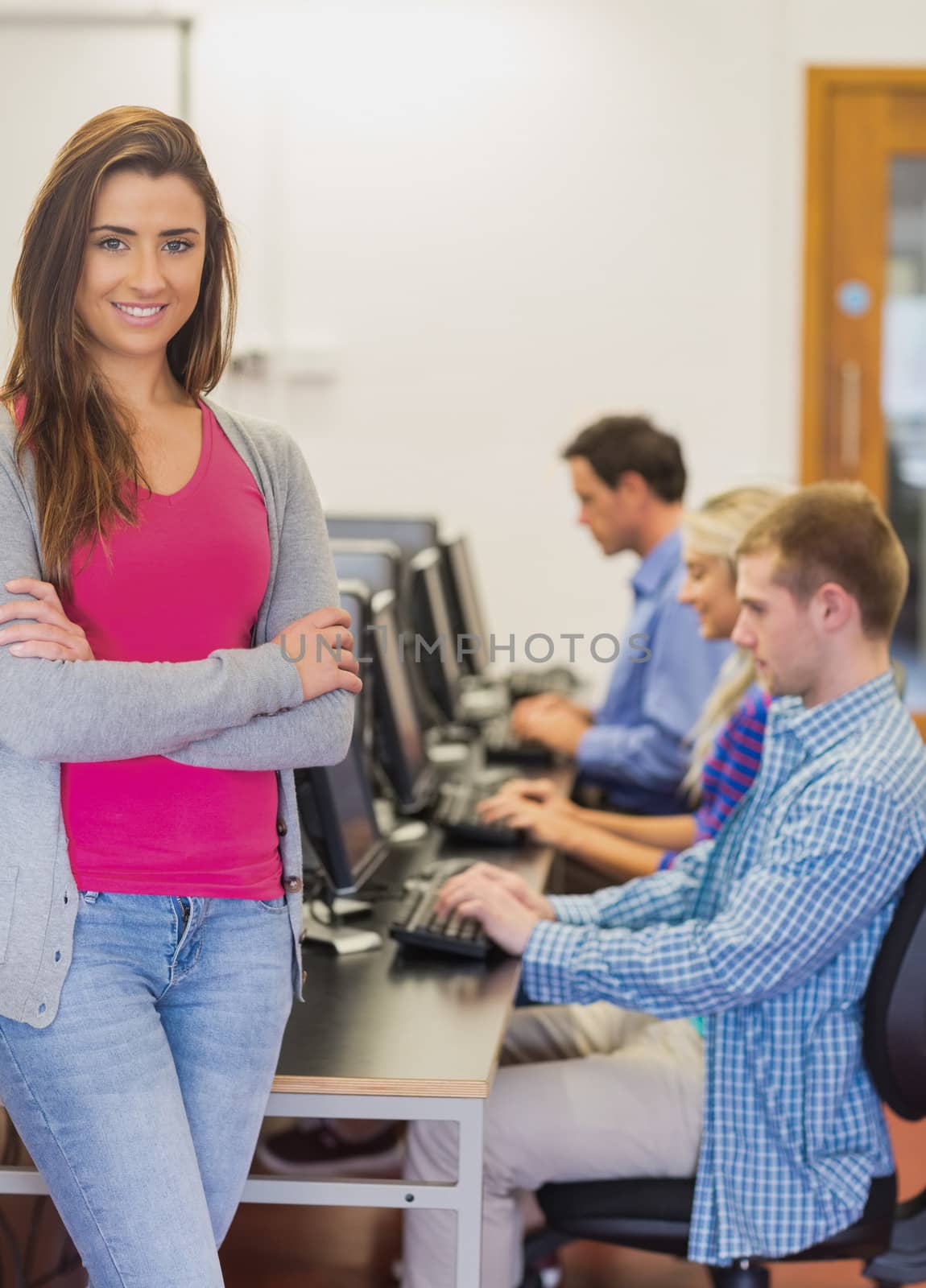 Portrait of a smiling teacher with young college students using computers in the computer room