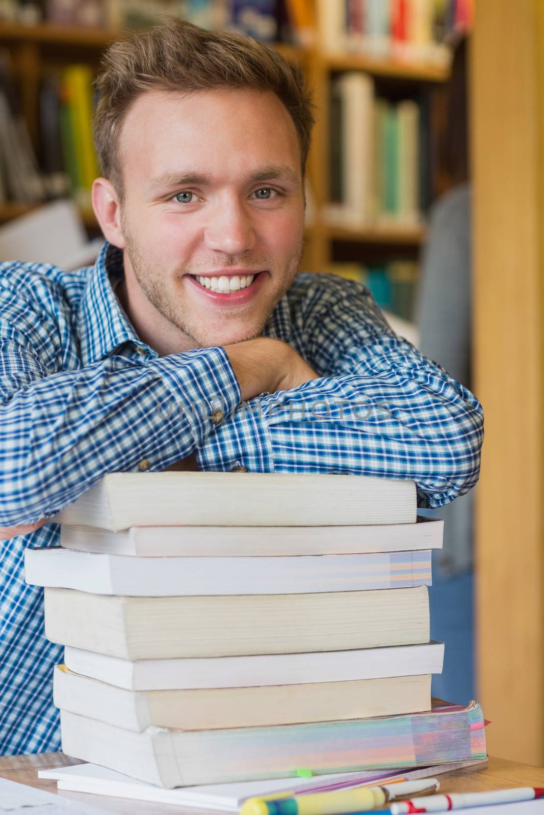 Male student with stack of books at library by Wavebreakmedia