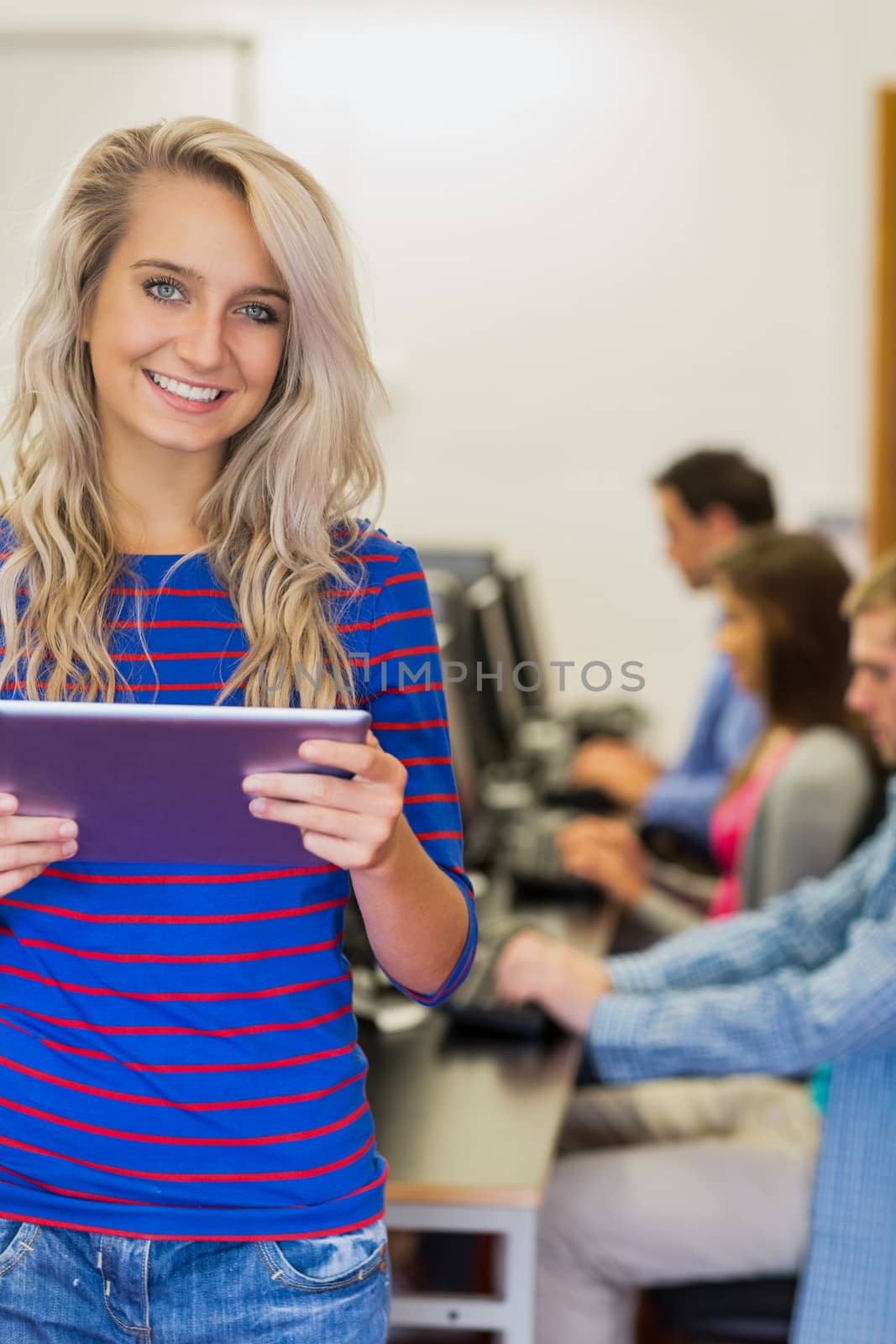 Teacher holding tablet PC with young college students using computers in the computer room