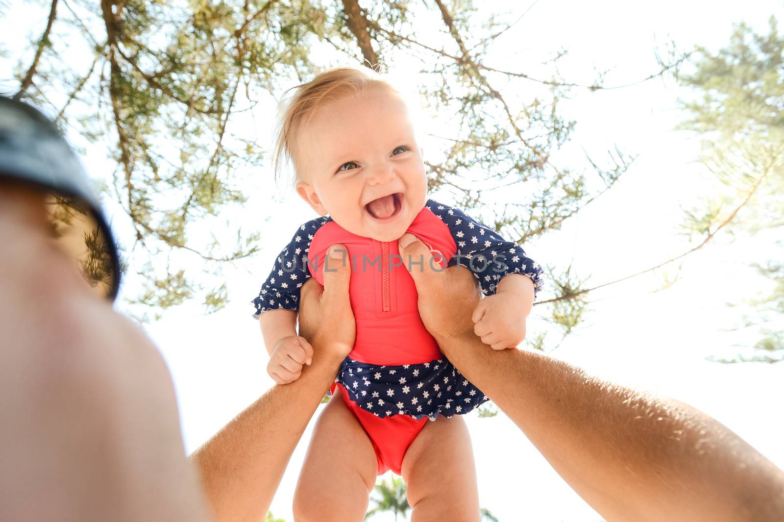 Happy baby girl in her prink and blue bathers in her fathers arms