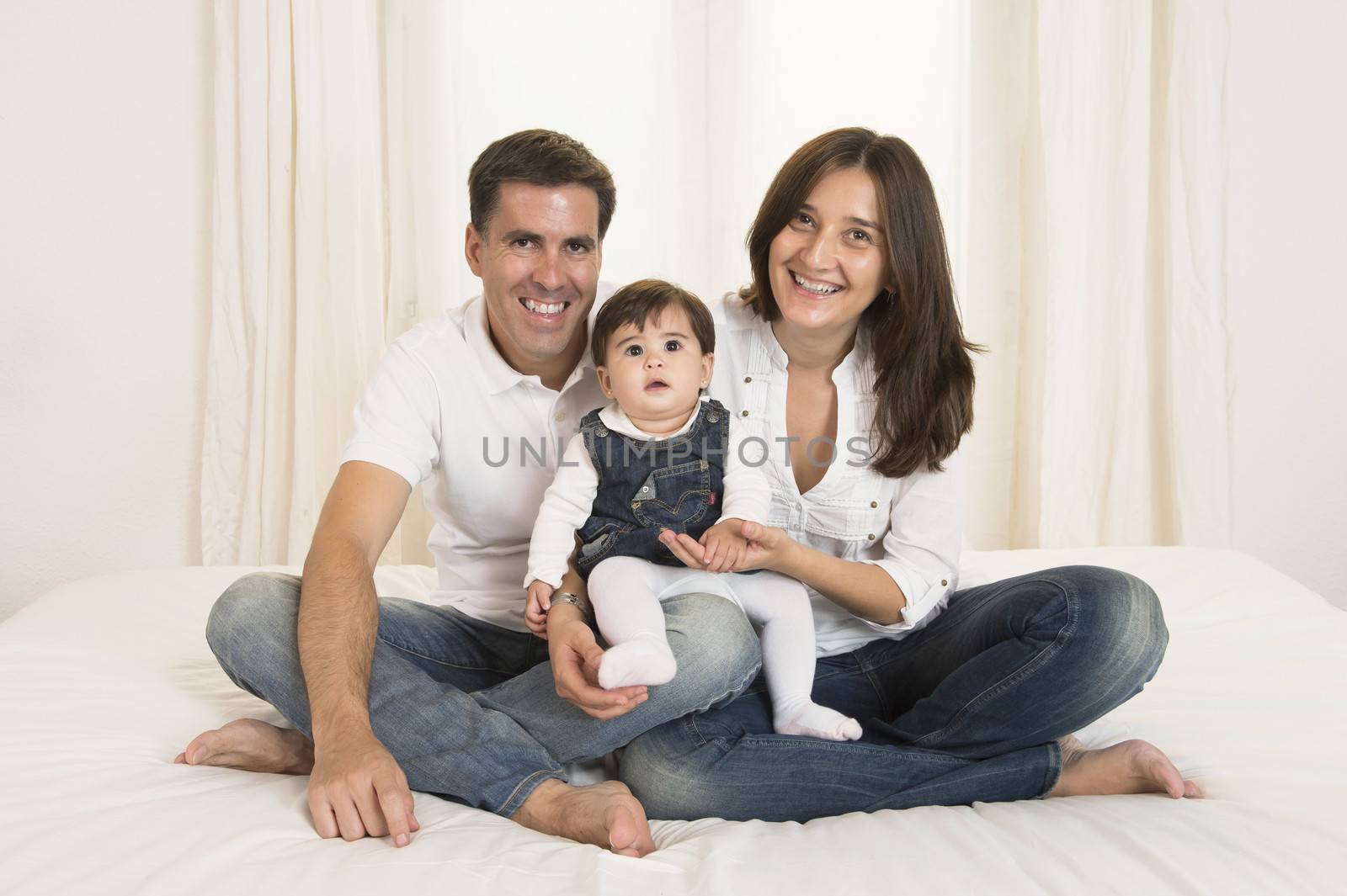 Young couple mother father and baby girl sitting on bed isolated portrait