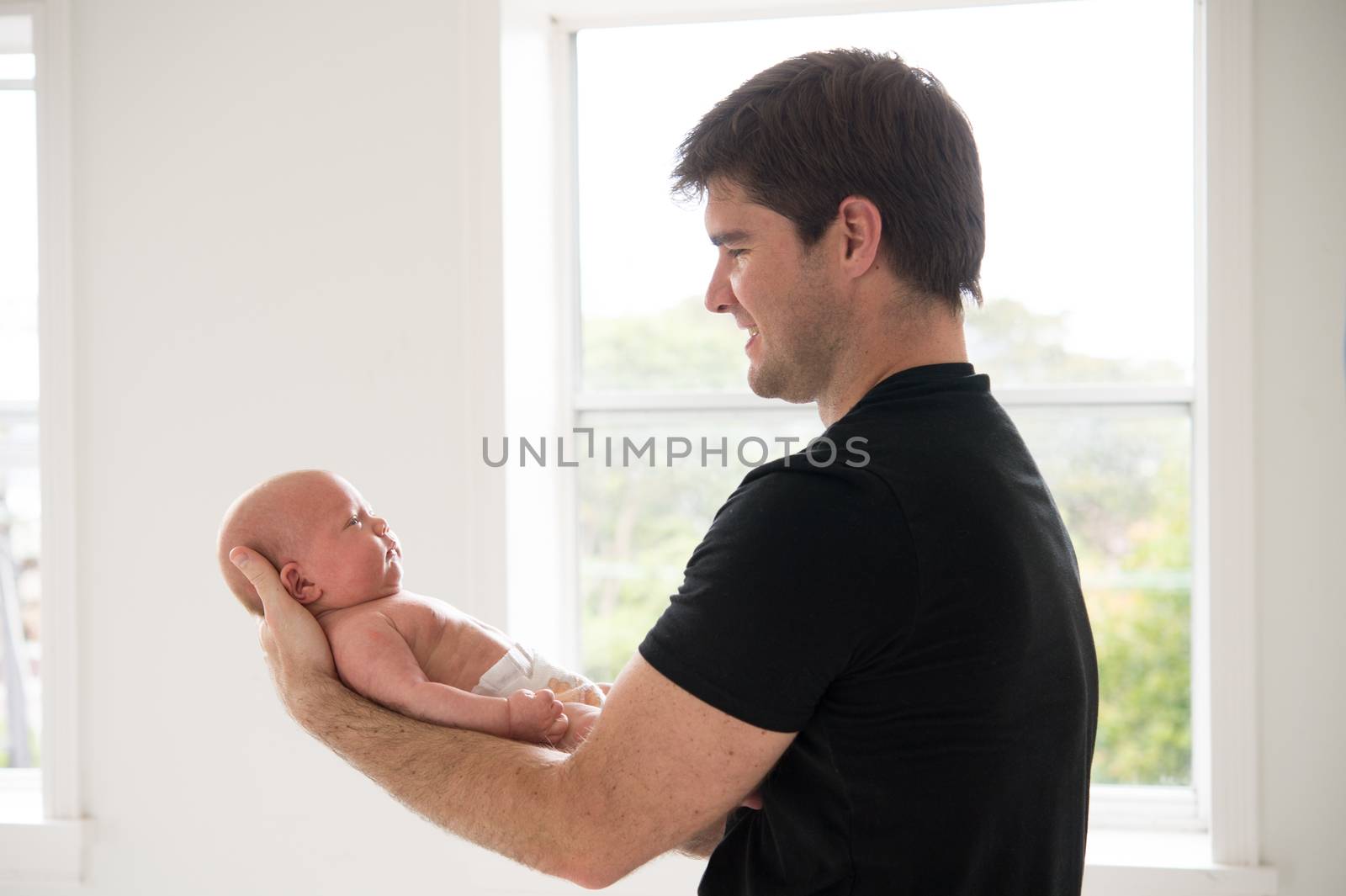 Father wearing black t shirt holding his 3 week old baby boy backlighting with white background
