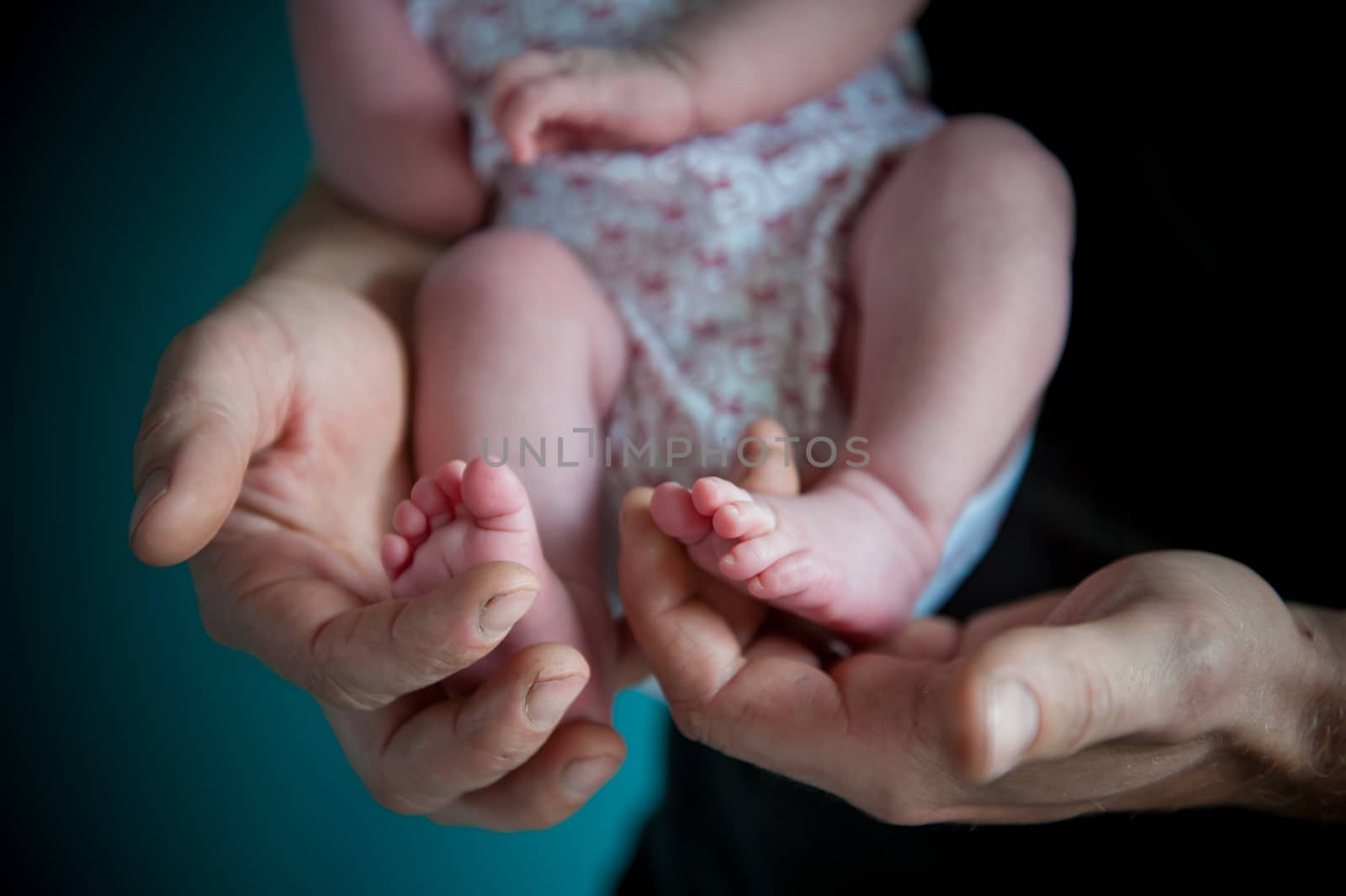 Father holding sweetly with his hands the tiny feet of his newborn lovely daughter