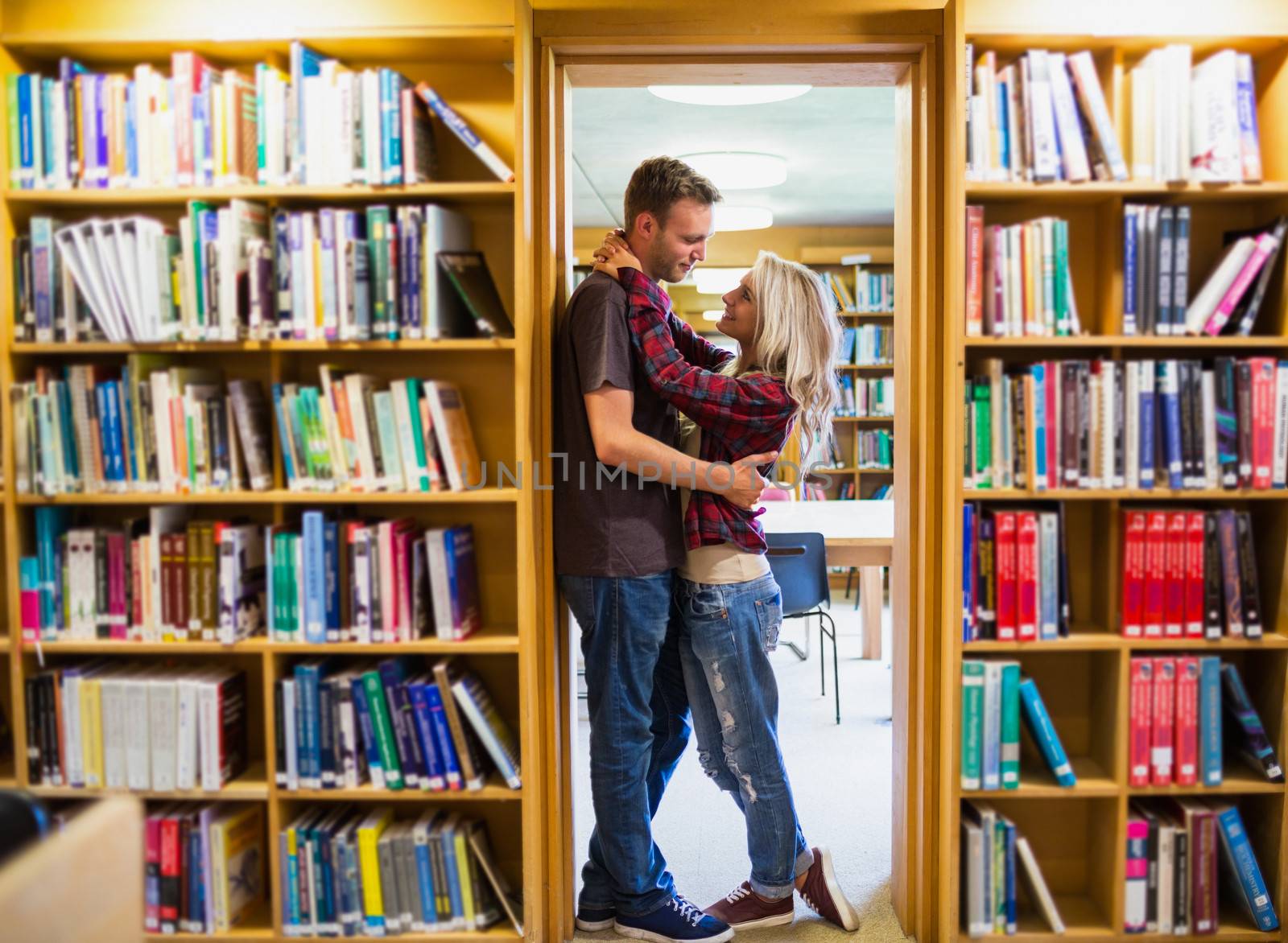 Full length side view of a young romantic couple embracing by bookshelves in the library