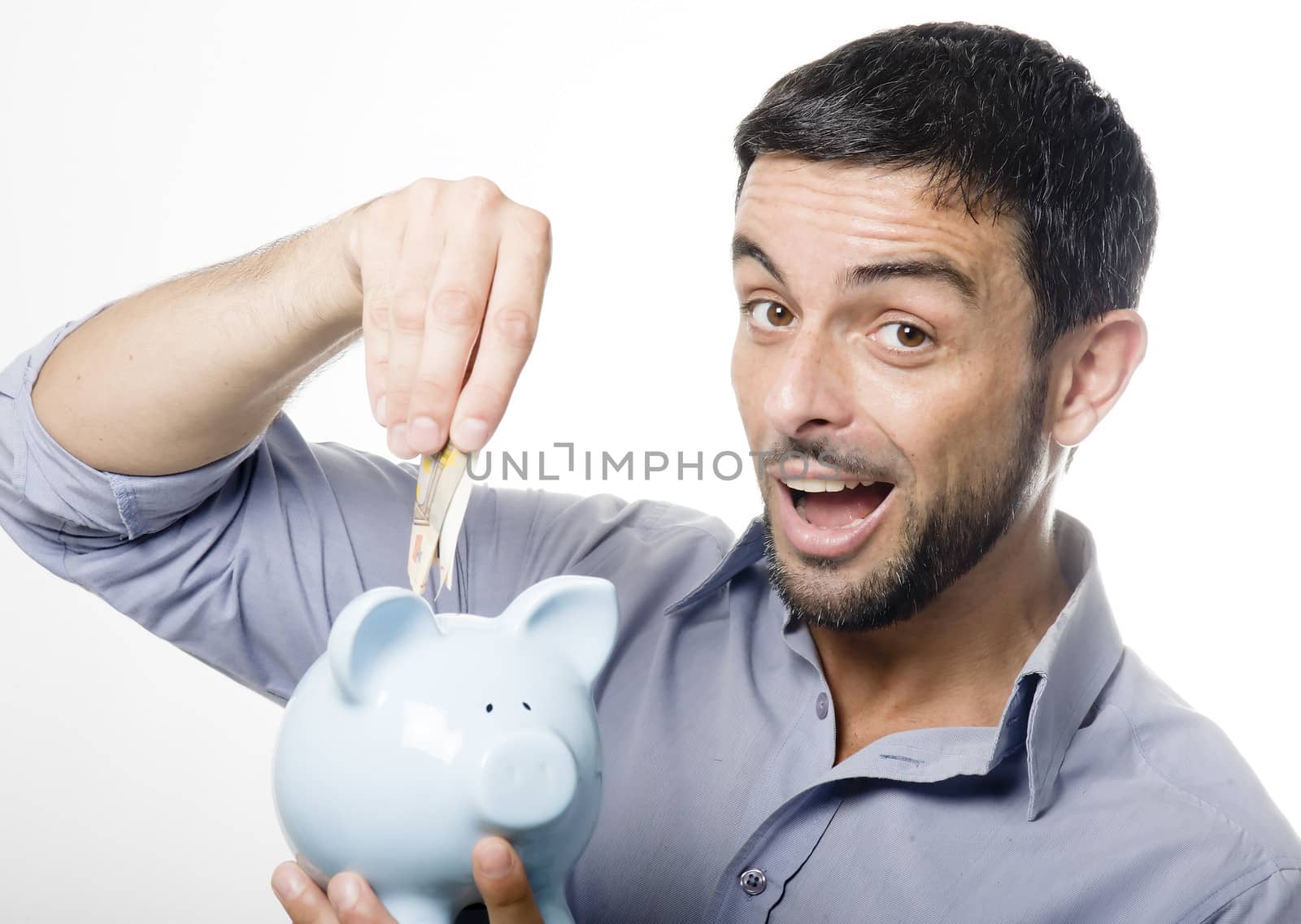 Handsome Young Man with Beard putting Money in Blue Piggy bank Isolated on White Background