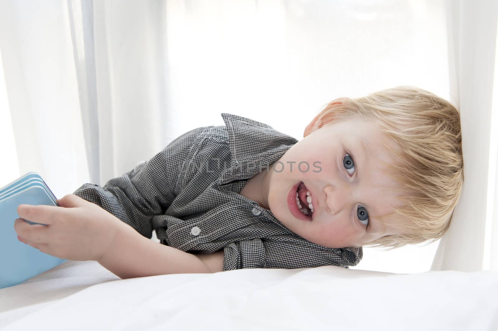 Cute little child lying on bed with book isolated on white background