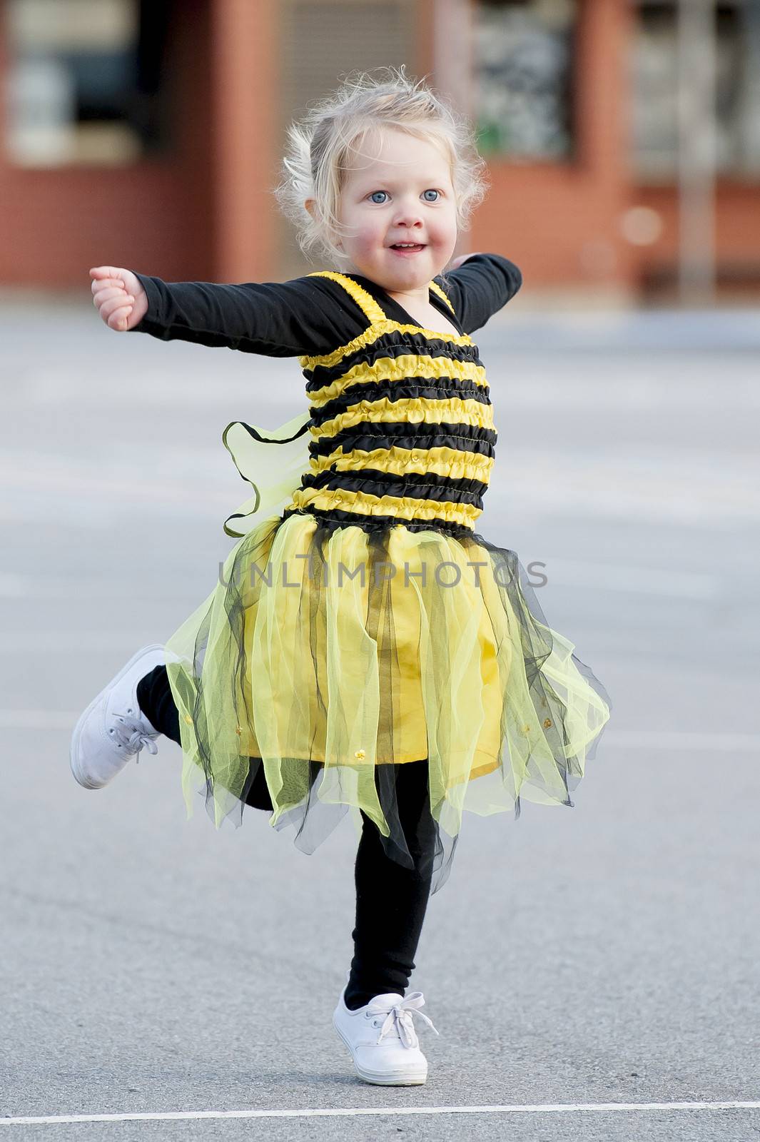 Little blond girl in bee costume dancing outdoors by ocusfocus