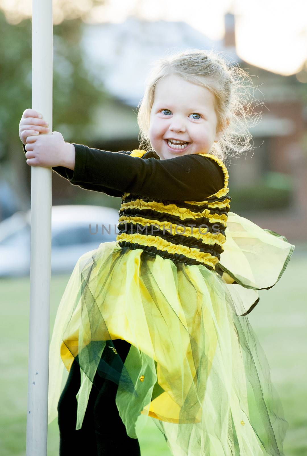 Happy blond little girl in bee costume dancing and playing outdoors