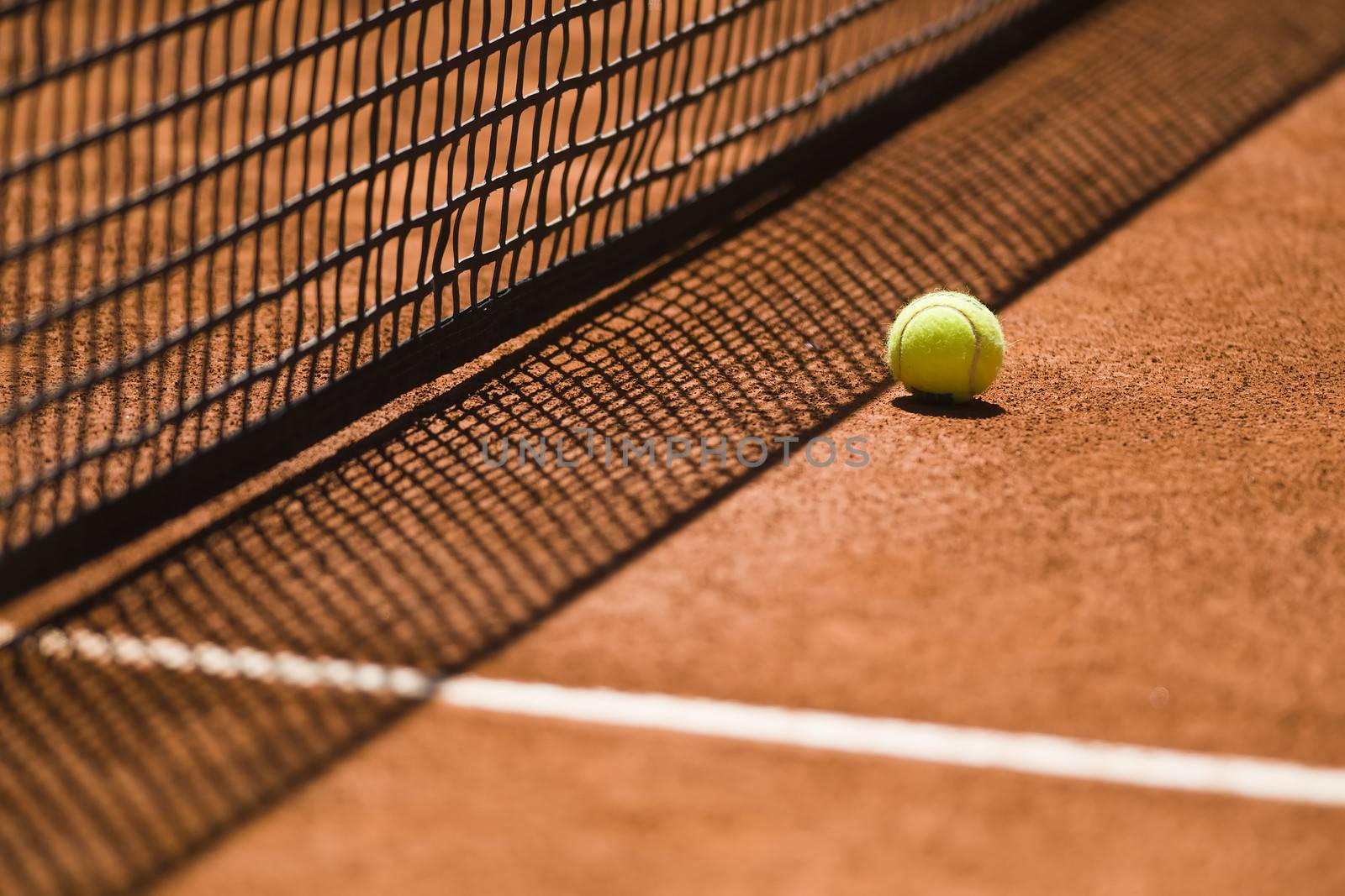 Tennis Ball and Net on a Clay Court by ocusfocus