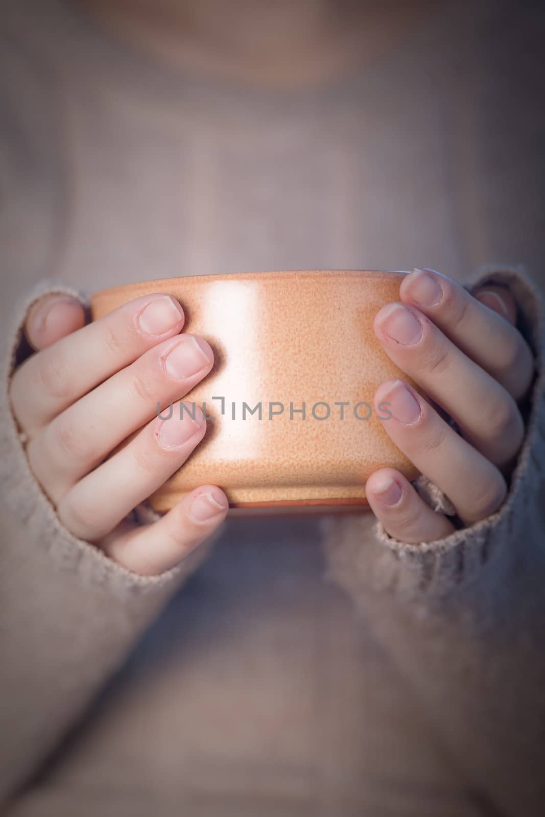 Hands of a woman in a brown jumper holding a cup of coffee.