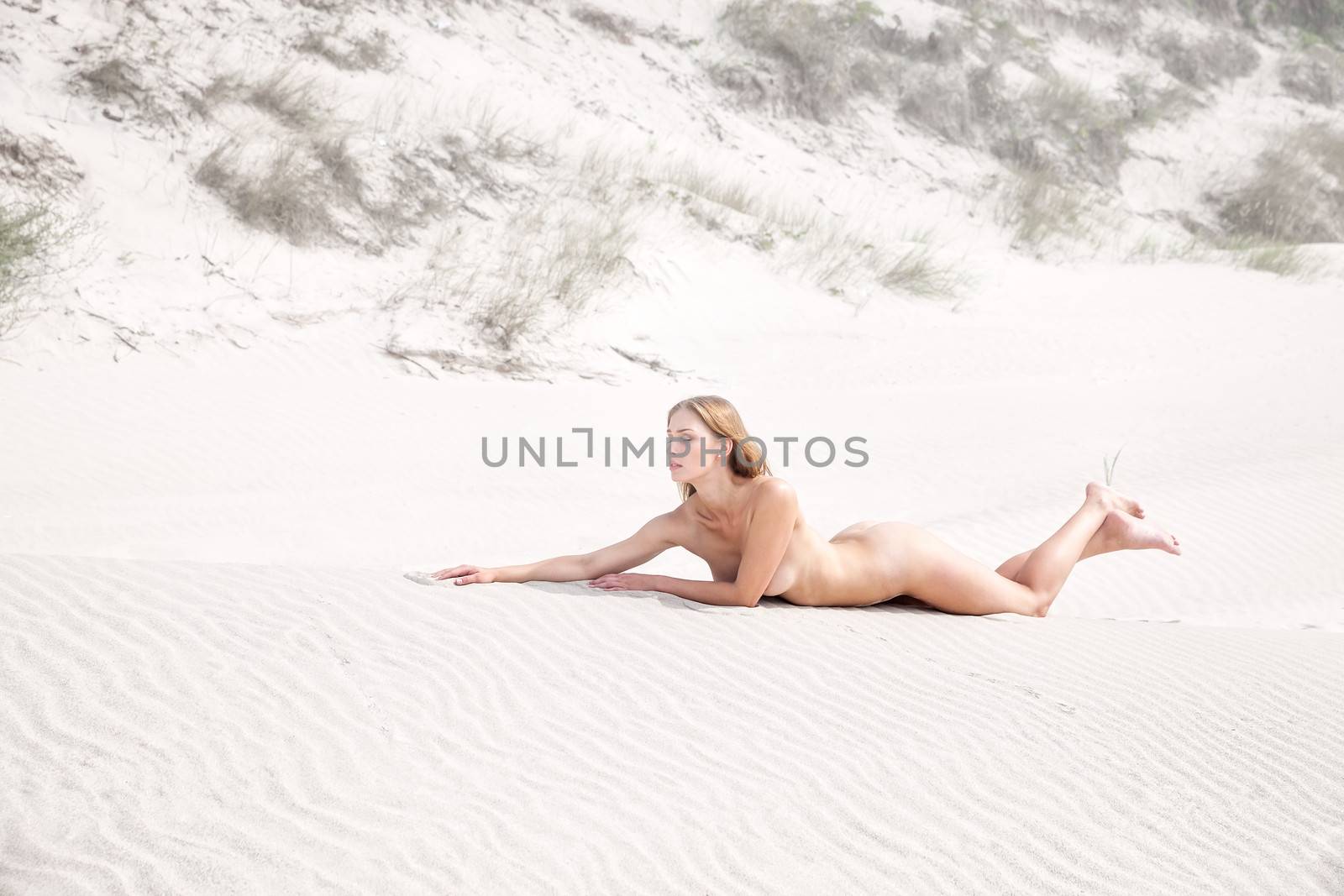 Young nude woman lying on a sandy beach on a foggy day