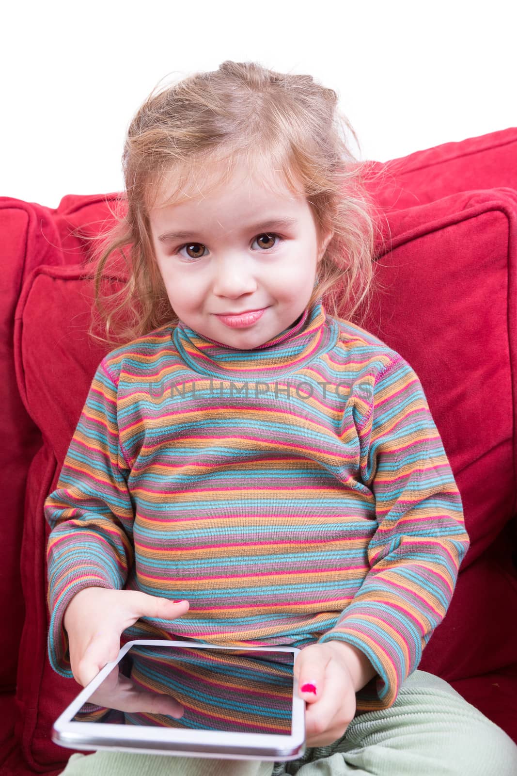 Cute pretty young girl with a tablet computer in her hands sitting on a red couch giving the camera a beautiful smile
