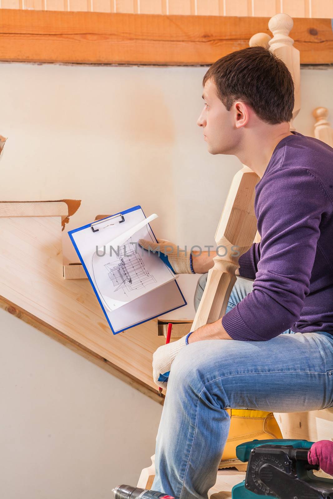 a young carpenter holding blueprint and sitting on ladder