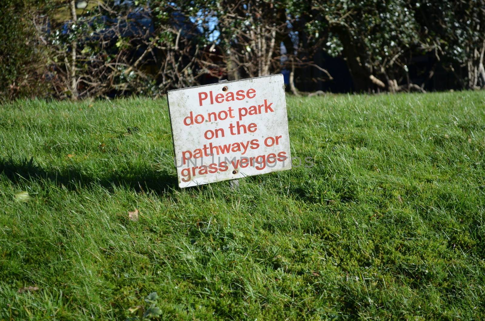 No parking sign on a verge beside a pathway asking for road users not to park on the grass.