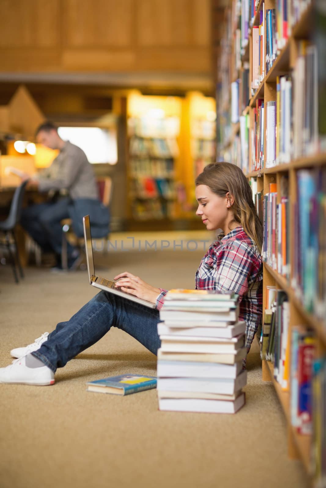 Pretty happy student using laptop on library floor at the university