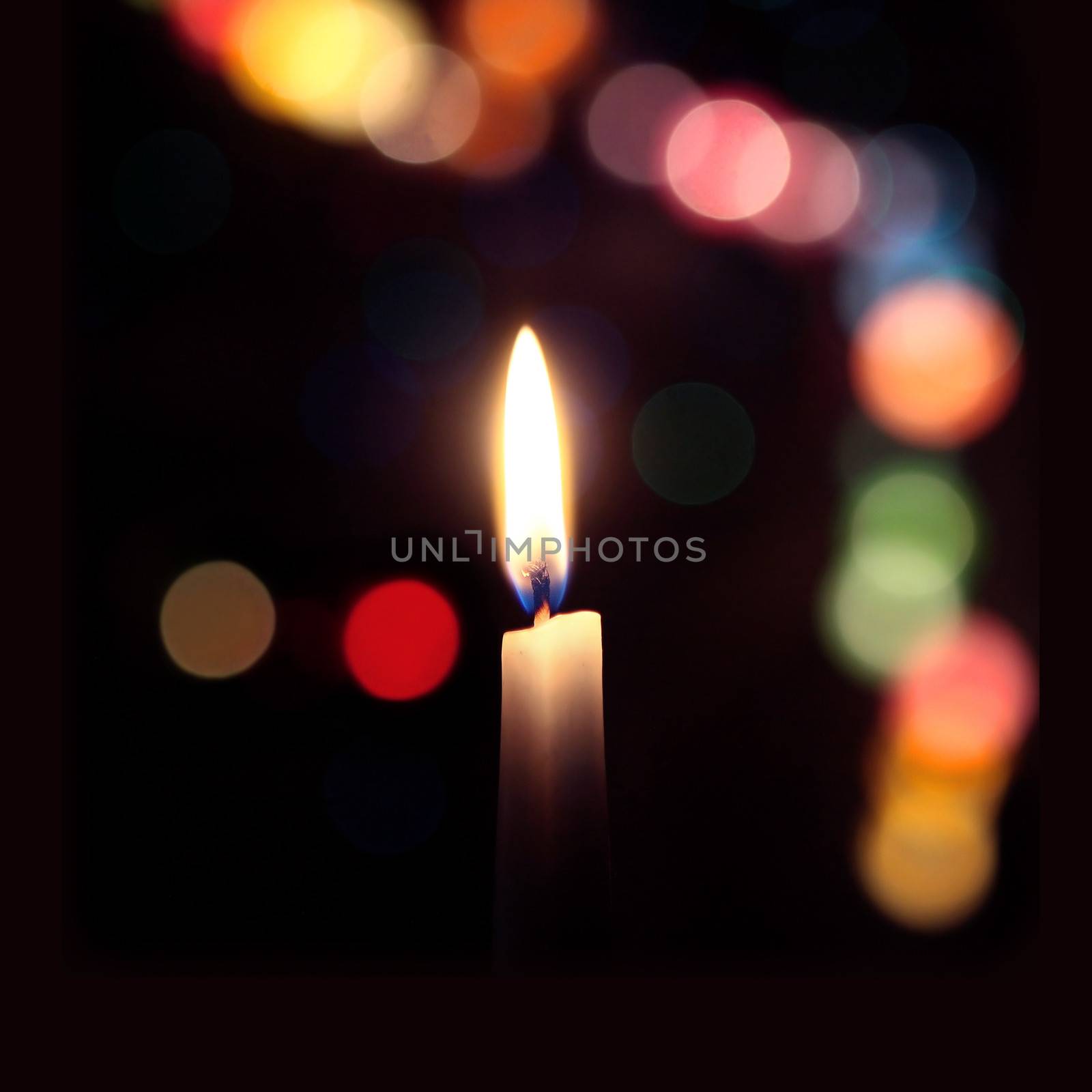 flame of a candle on a dark background with colored bokeh