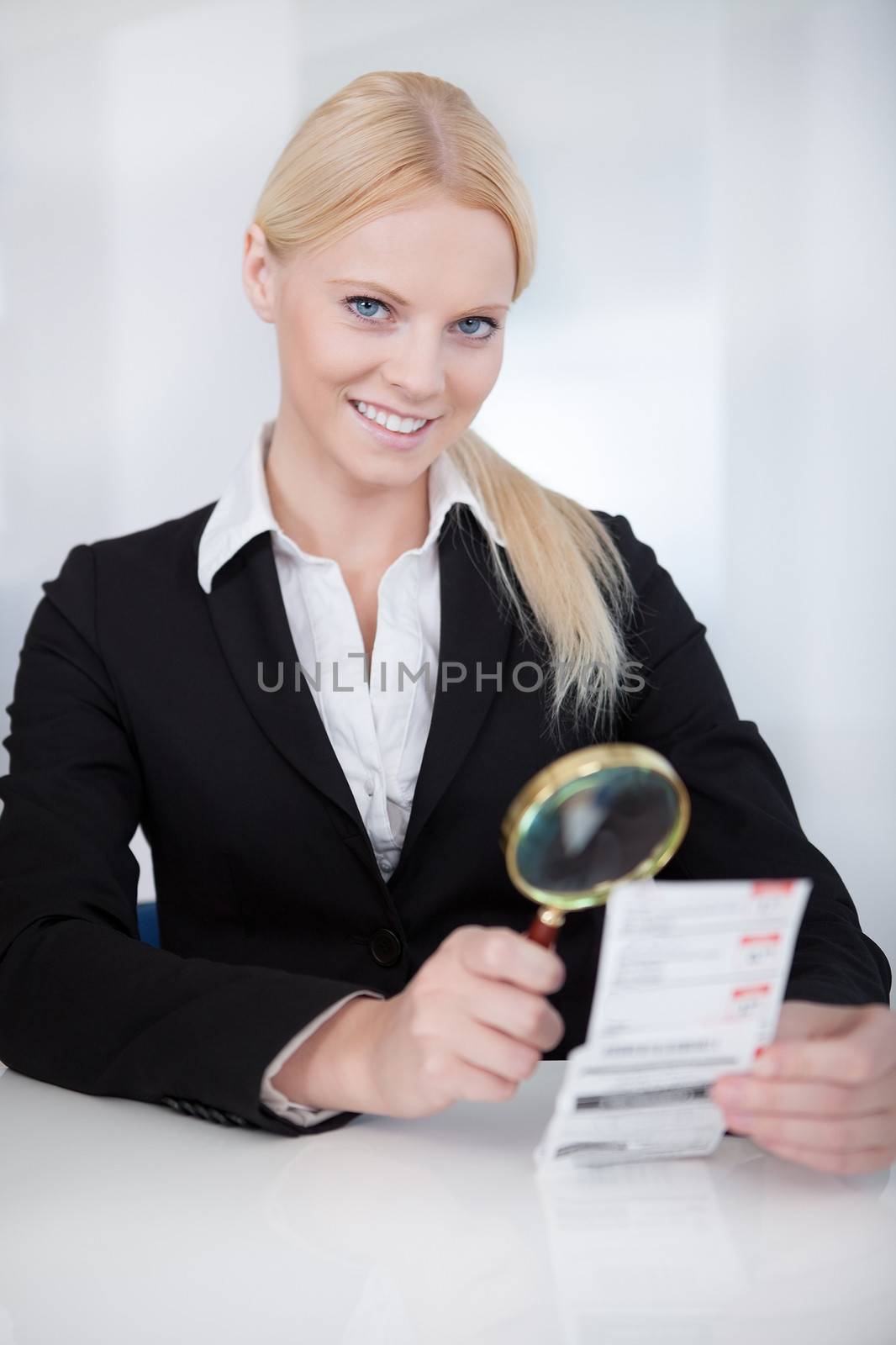 Cheerful businesswoman looking at check trough the loupe