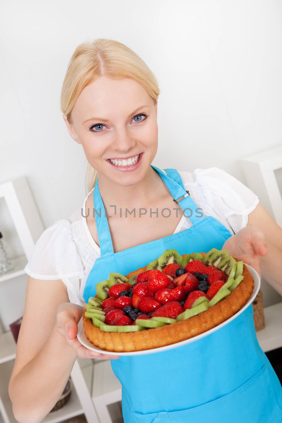 Beautiful young woman holding self-made cake in the kitchen