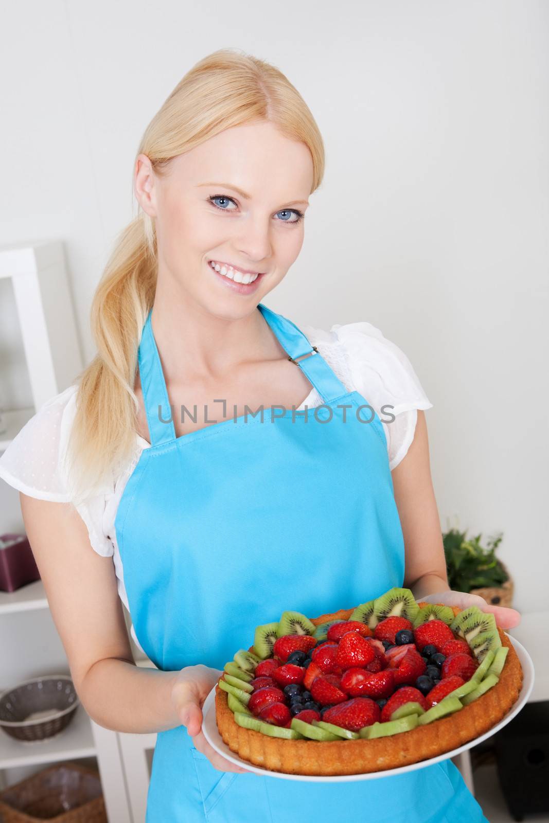 Beautiful young woman holding self-made cake in the kitchen