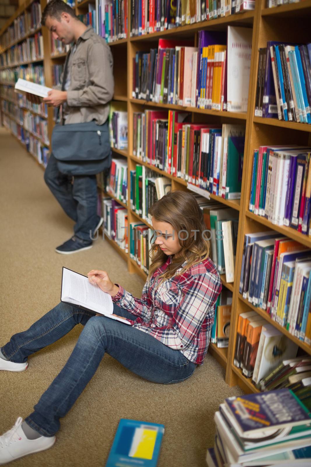 Concentrating student reading book on library floor at the university