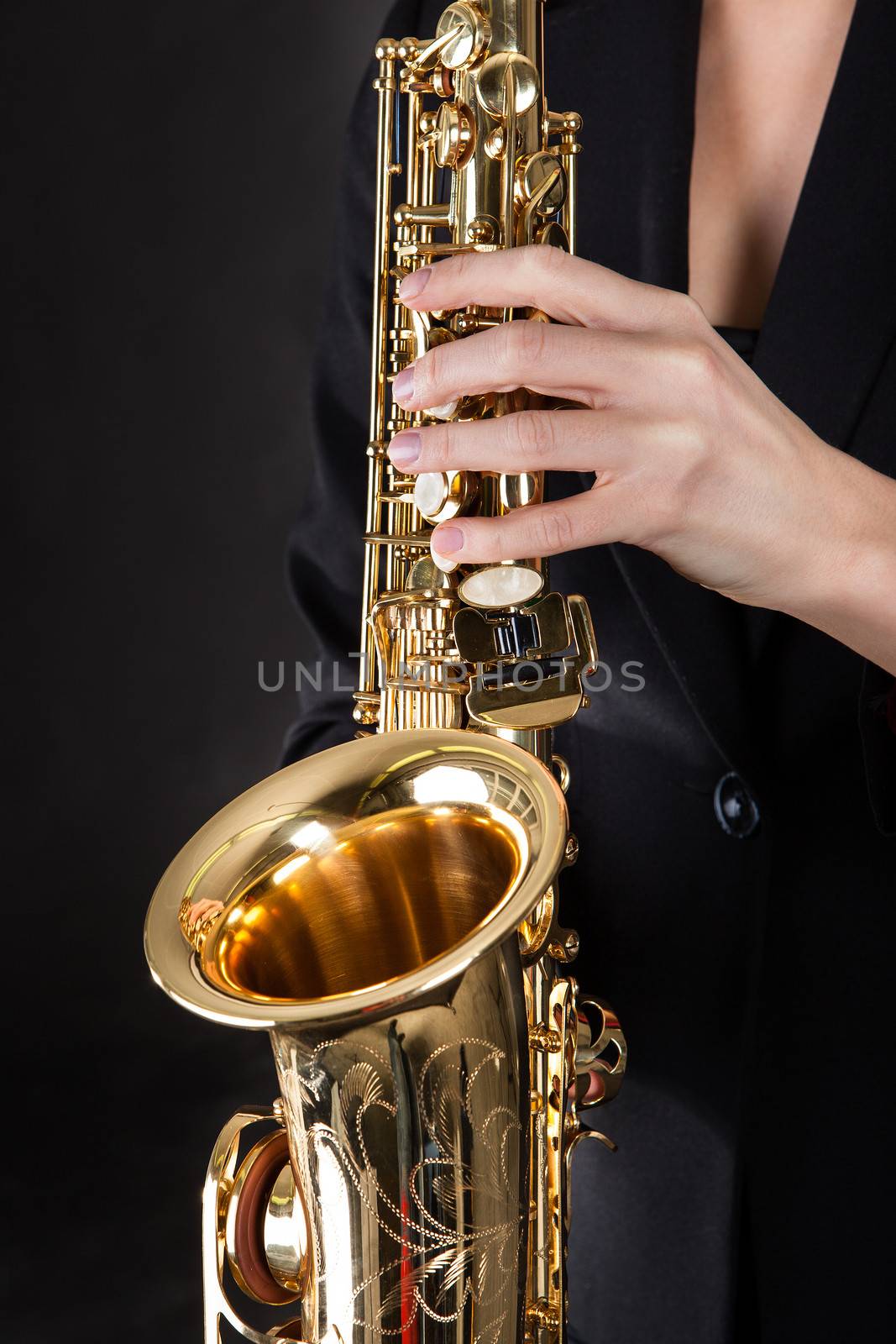 Beautiful young woman playing saxophone over black background