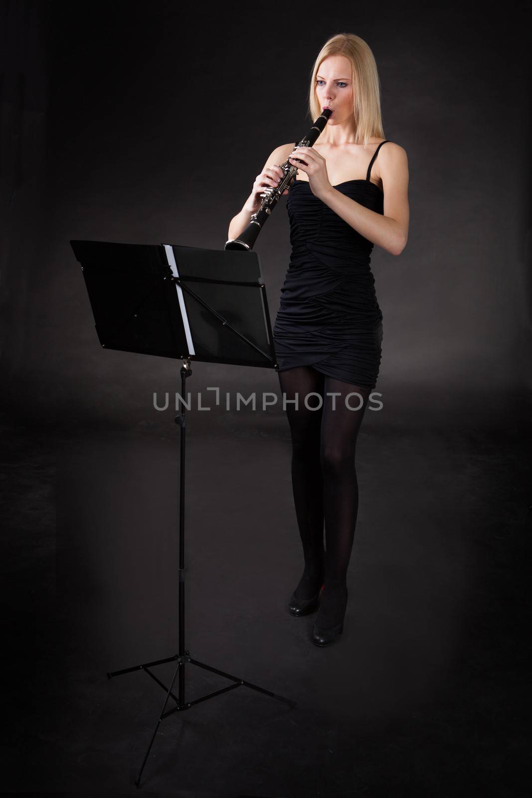 Beautiful young woman playing clarinet over black background