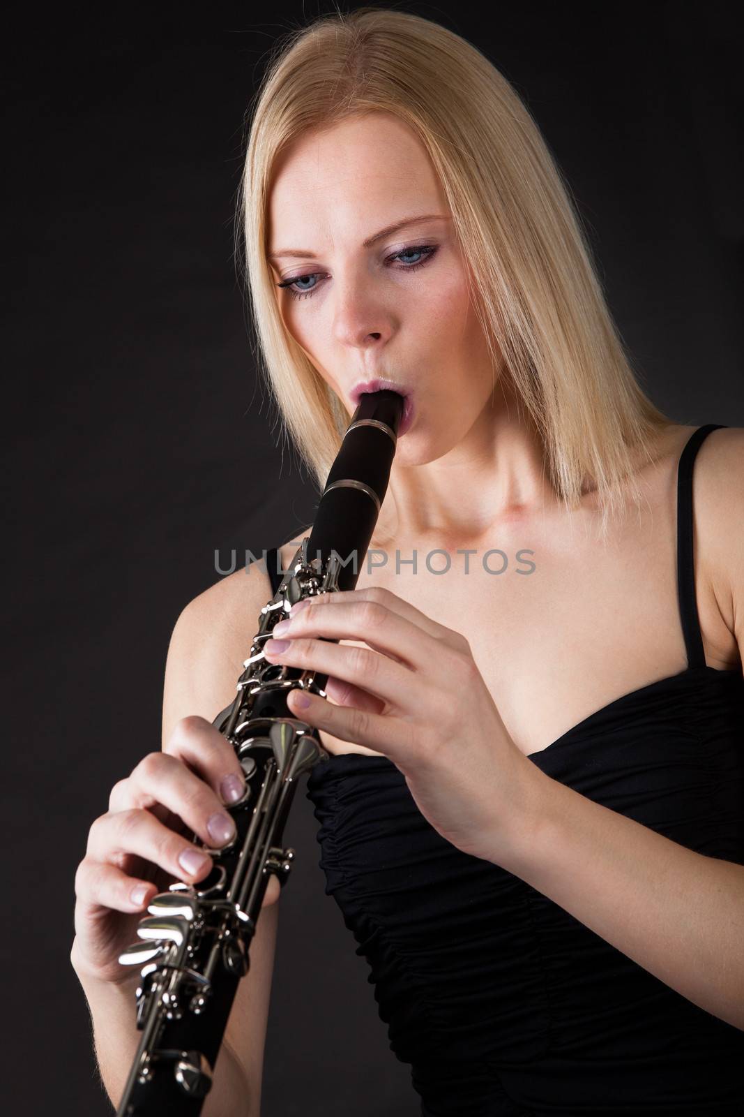 Beautiful young woman playing clarinet over black background