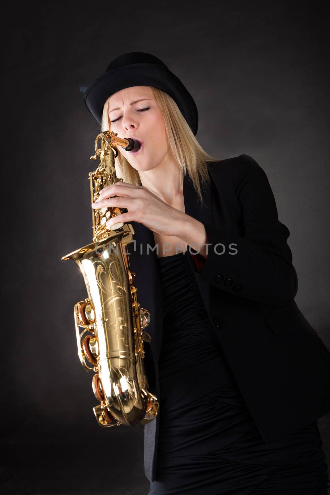 Beautiful young woman playing saxophone over black background