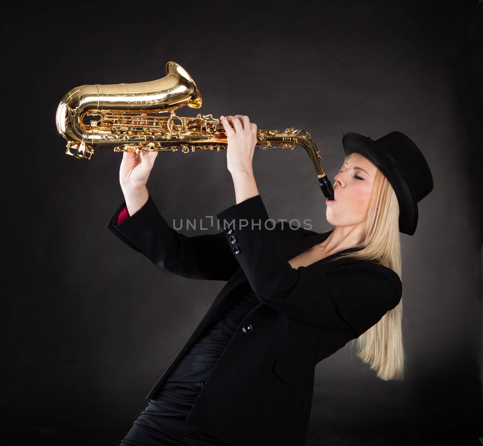 Beautiful young woman playing saxophone over black background