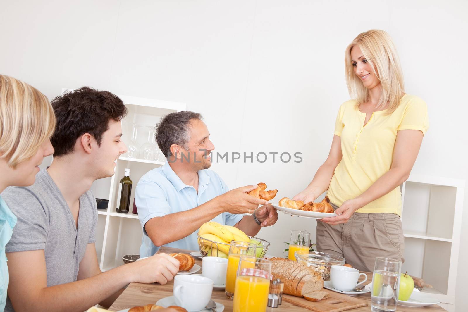 Young healthy family seated at the table being served croissants for breakfast by the smiling mother